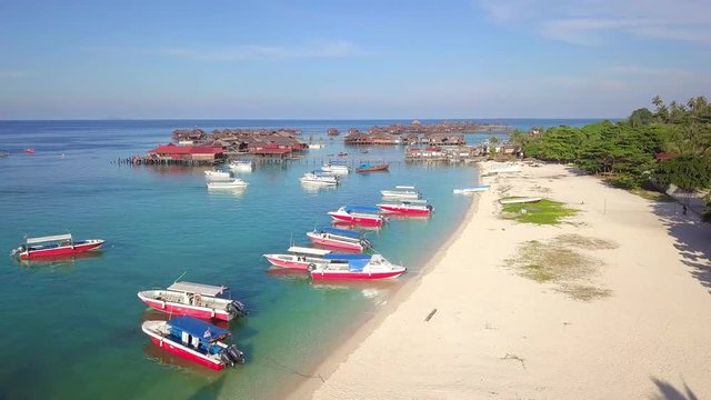 Aerial flight over tropical beach towards boats and huts in Mabul, Malaysia