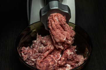 The cook grinds meat in minced meat on an electric meat grinder