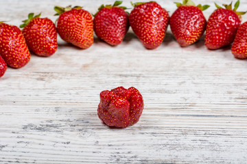 An arc of fresh ripe red strawberries lies on a light textured wooden table. Flatlay, Copyspace