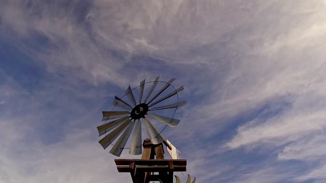 old cowboy, farm and prairie style wind pump spinning against a blue sky