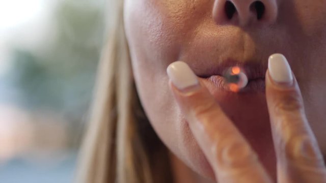 Slow motion close-up of a woman's lips as she smokes a cigarette and lows smoke towards camera creating a white out effect