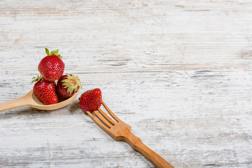 Summer vitamin food. Lots of fresh ripe fragrant strawberries and a wooden spoon and fork, lie on a...