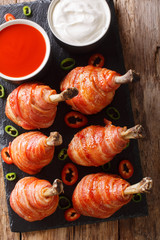 Spicy Lollipops fried chicken legs wrapped in bacon served with sauces close-up on a slate board. Vertical top view