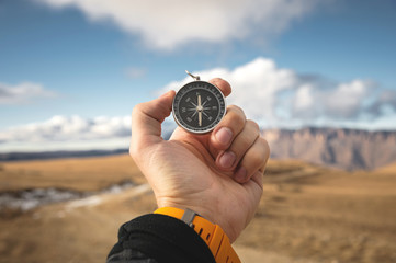 A male Hiker is looking for a direction with a magnetic compass in the mountains in the fall. Point...