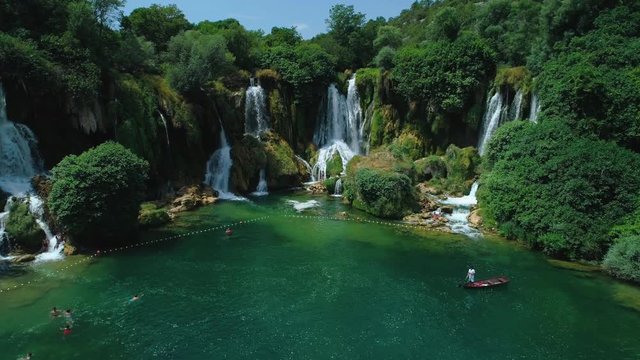 Aerial fly by of the dramatic waterfall Kravica in Bosnia and Herzegovina during a beautiful day in the summer. People are swimming in the water.