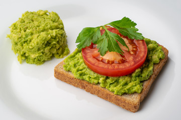 Avocado toast with a slice of tomato and chopped avocado pulp on a white plate
