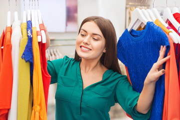 fashion, shopping and people concept - happy woman choosing clothes in clothing store