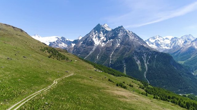 Aerial shot flying above descending track in the grass field. High mountains in the background
(Val d'H&radic;&copy;rens, Valais, Switzerland)