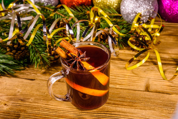 Cup of mulled wine with cinnamon, christmas decorations and fir tree branches on wooden table