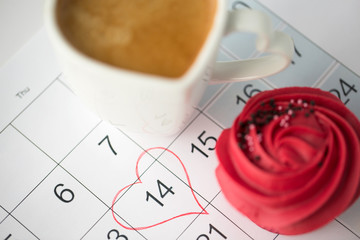 valentines day and holidays concept - close up of calendar sheet with 14th february date marked by heart shape, coffee cup and cupcake