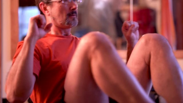 Extreme closeup of mature man balancing and doing leg crunches in a rowing manner for ab exercises in an indoor workout area.