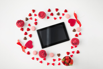 valentines day and technology concept - tablet pc computer, frosted cupcakes, red heart shaped chocolate candies, macarons and strawberries