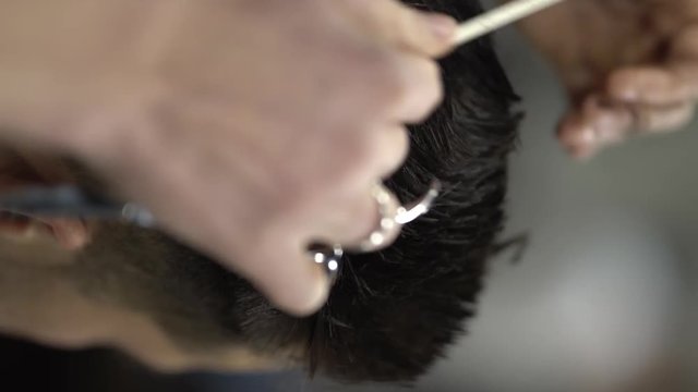 Barberman cutting vet black hair of a man using a white comb and scissors. Close-up concept. Vertical position. Detailed shooting