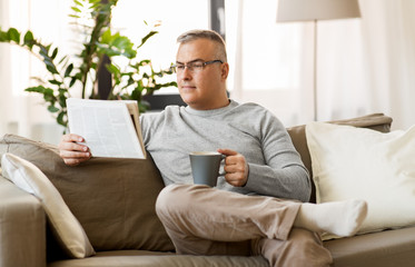 leisure, information, people and mass media concept - man reading newspaper and drinking coffee at home