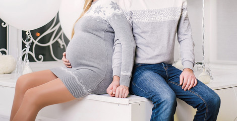 Happy pregnant woman and her husband sitting on stairs, holding hands and touching belly, copy space. Pregnancy and expectation concept