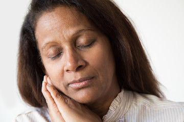 Closeup of serene sleepy Latin woman. Middle aged lady with closed eyes placing hands under cheek. Falling asleep concept