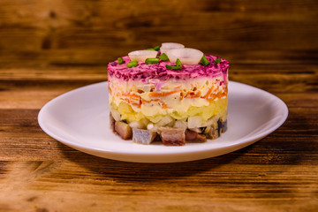 White plate with russian traditional new year salad herring under fur coat on wooden table