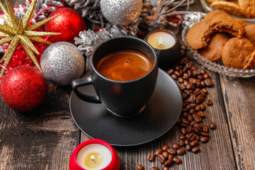 Black cup of coffee, cookies filled with chocolate, Christmas balls, candles and coffee beans. Close-up on the old rustic wooden table