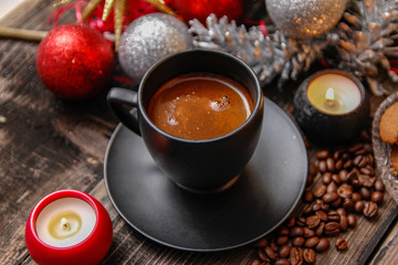 Black cup of coffee, cookies filled with chocolate, Christmas balls, candles and coffee beans. Close-up on the old rustic wooden table