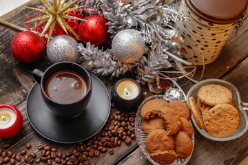 Black cup of coffee, cookies filled with chocolate, Christmas balls, candles and coffee beans. Close-up on the old rustic wooden table