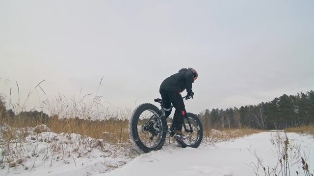 Professional extreme sportsman biker riding fat bike in outdoors. Close-up view of rear wheel. Cyclist ride in winter forest. Man on mountain bicycle with big tire. Snow fly into the lens camera.