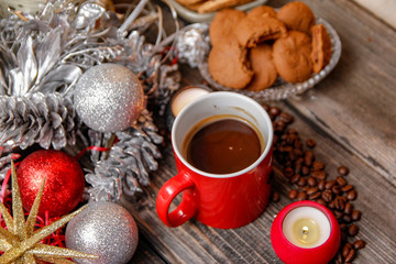 Big red cup of coffee, cookies filled with chocolate, Christmas balls, candles and coffee beans. Close-up on the old rustic wooden table