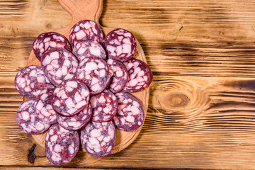 Cutting board with sliced salami sausage on a wooden table. Top view