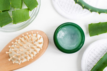 Small green jar with aloe vera healing balm (salve, ointment, facial cream or hair mask) and wooden hair brush. Natural beauty treaments and spa. White background. Top view, copy space. 