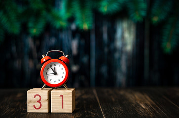 December 31st set on wooden calendar with red alarm clock on dark blured background.