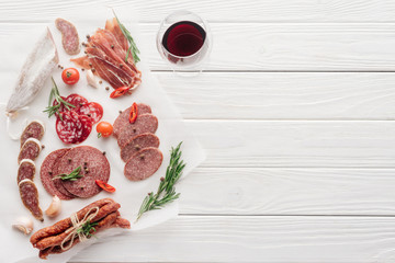 food composition with glass of red wine and assorted meat snacks on white wooden tabletop