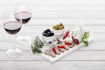 close up view of tasty meat appetizers and glasses of red wine on white wooden surface