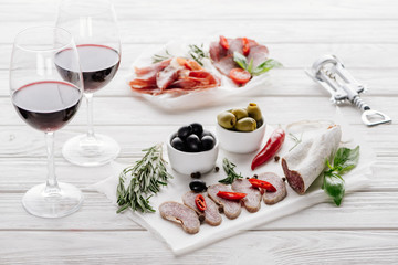 close up view of tasty meat appetizers and glasses of red wine on white wooden surface