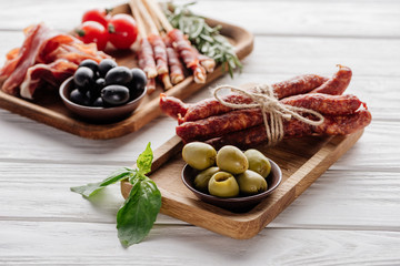 food composition with various meat appetizers, olives and basil leaves on white wooden surface