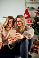 Beautiful friends/sisters enjoying Christmas eve/New year while using cellphone.