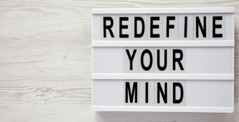 'Redefine your mind' words on modern board over white wooden surface, top view. Overhead, flat lay, from above. Space for text.