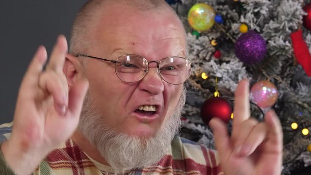happy elderly man grimaces and actively expresses his emotions against background of Christmas tree in garlands, green UFO balls, proton purple toy, plastic pink angel, neon glow