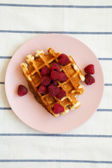 Traditional belgian waffle with raspberries on pink plate on cloth, top view. Flat lay, overhead, from above.