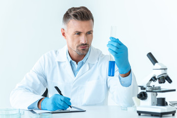 handsome scientist looking at test tube with blue reagent isolated on white