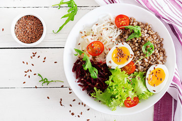 Buckwheat porridge buddha bowls with beetroot, cabbage, boiled eggs and  fresh tomato on white table. Healthy breakfast. Top view