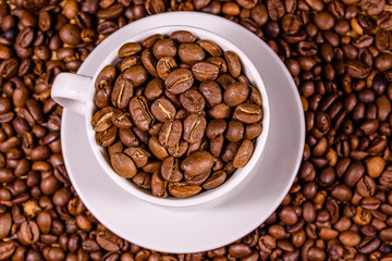 White cup filled with coffee beans on wooden table. Top view