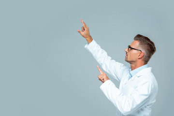 side view of handsome scientist in glasses moving something isolated on grey, artificial...