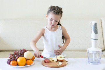 The child cuts apples with a knife. The girl cuts with a knife the fruit for making juice.