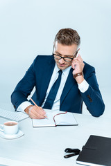high angle view of handsome businessman writing something and talking by smartphone isolated on white