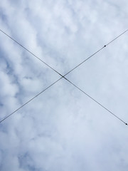 Electrical wires in the air in the shape of X against cloudy sky.