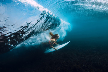 Attractive surfer woman dive underwater, under barrel wave in blue ocean