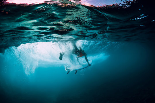 Attractive surfer woman dive underwater with under barrel wave.