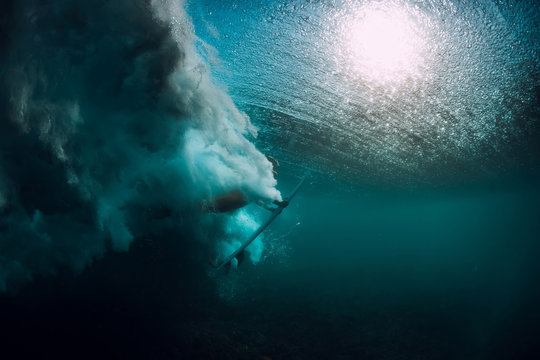 Surfer with surfboard dive underwater with under wave.