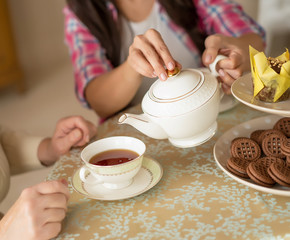 Hands of young woman with white china teapot pouring tea into cup of her senior mother
