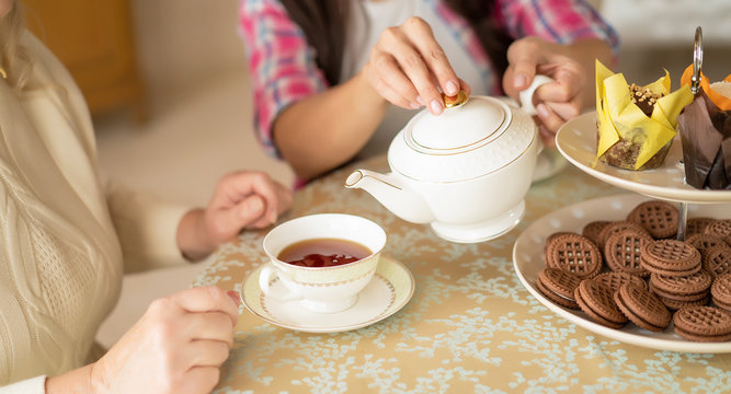 Hands of young woman with white china teapot pouring tea into cup of her senior mother - Powered by Adobe
