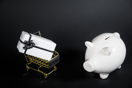 Piggy bank and gift box in shop cart isolated on black background.
